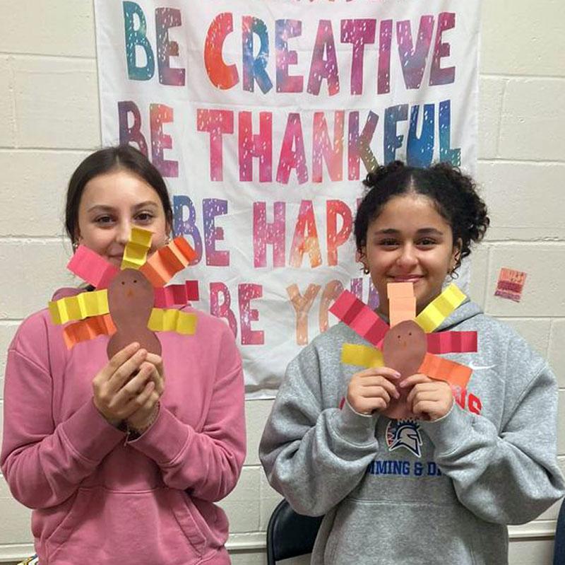 Two children hold up paper turkeys